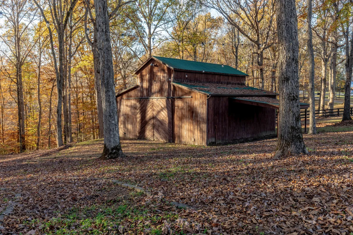 A rustic wooden barn surrounded by leafy trees and a carpet of fallen leaves, evoking the beauty of the outdoors and the opportunity for nature walks, photography, or picnics.