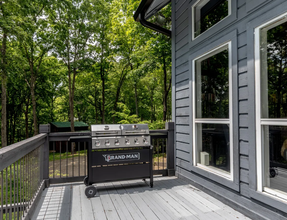 A spacious wooden deck outfitted with a barbecue grill and surrounded by towering trees, with ample room for outdoor dining and relaxation. The deck captures the essence of alfresco meals and sociable, seasonal gatherings.