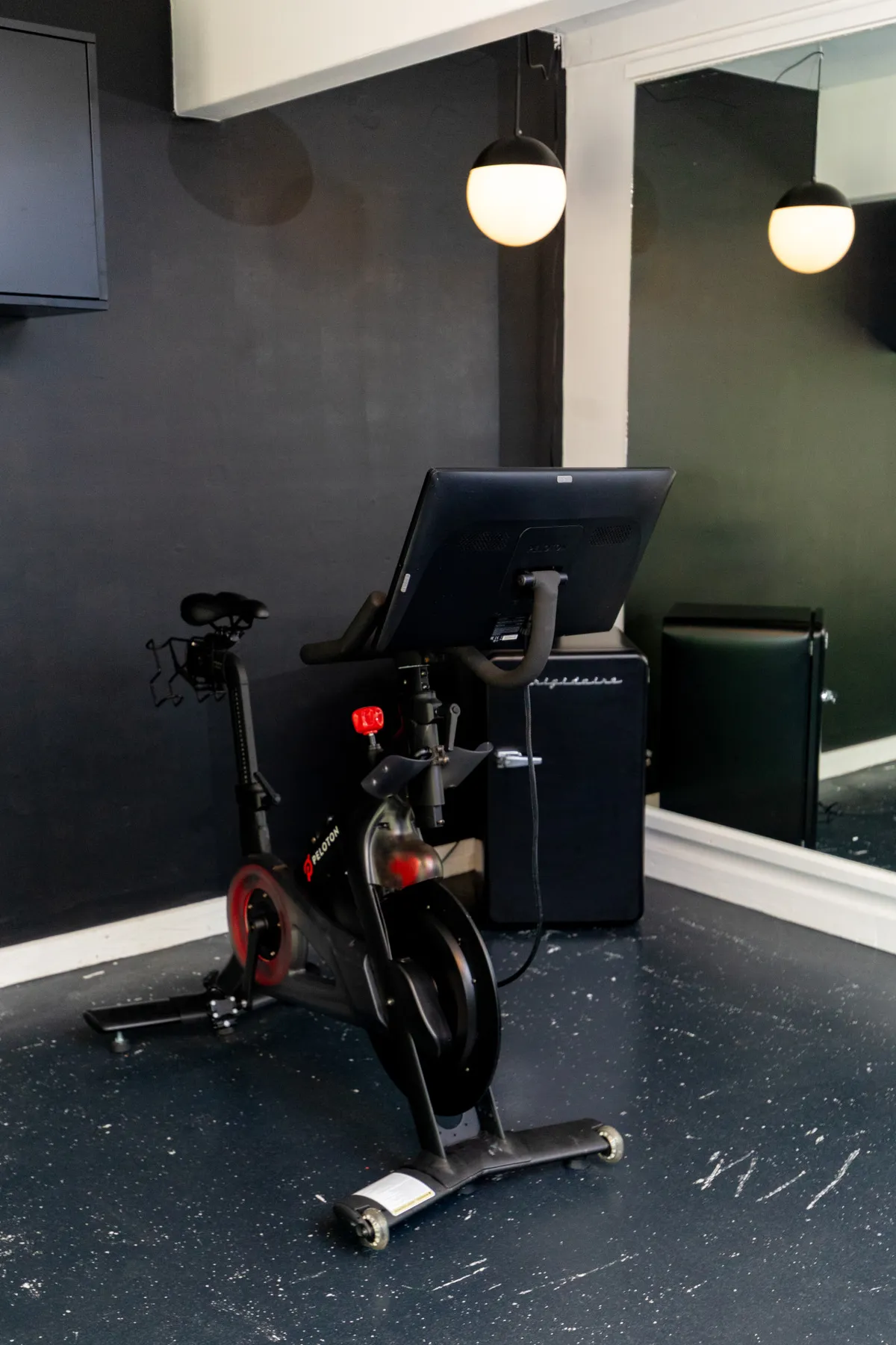A home gym setup with an exercise bike (similar to a Peloton), large wall mirror for feedback during workouts, and ambient lighting that creates an energetic and motivating vibe.