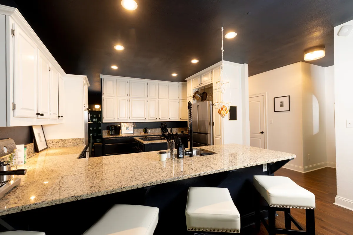 A bright, contemporary kitchen featuring a granite countertop, white cabinetry, bar stools, and a spacious kitchen island. The open layout is ideal for cooking, entertaining, and socializing, with ample space for guests to gather around during meals or celebrations.