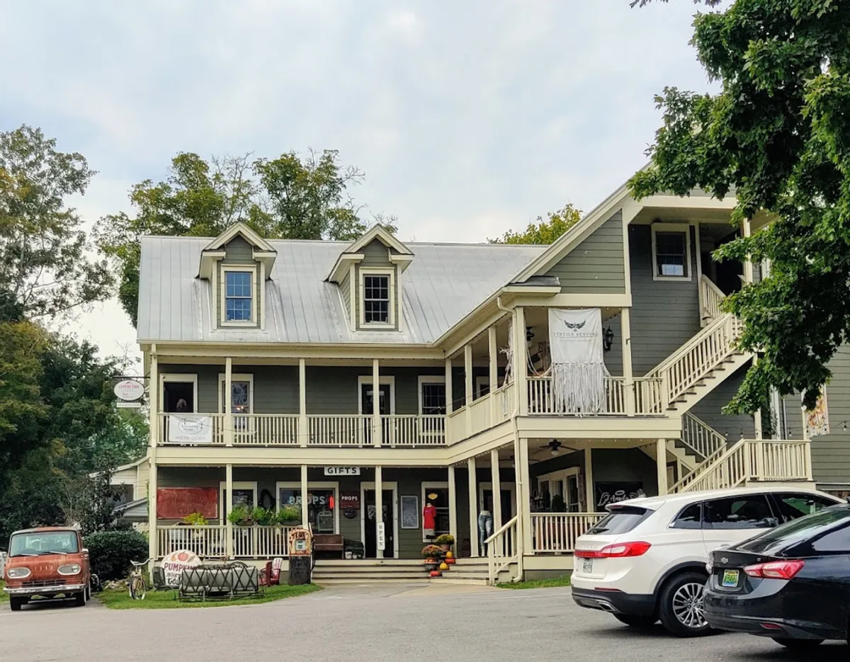 The photo captures the inviting exterior of a charming boutique with a prominent 'GIFTS' sign, a sprawling wraparound porch, and balconies. Visitors are seen enjoying the outdoor space, hinting at the village’s quirky shops and relaxed pace.