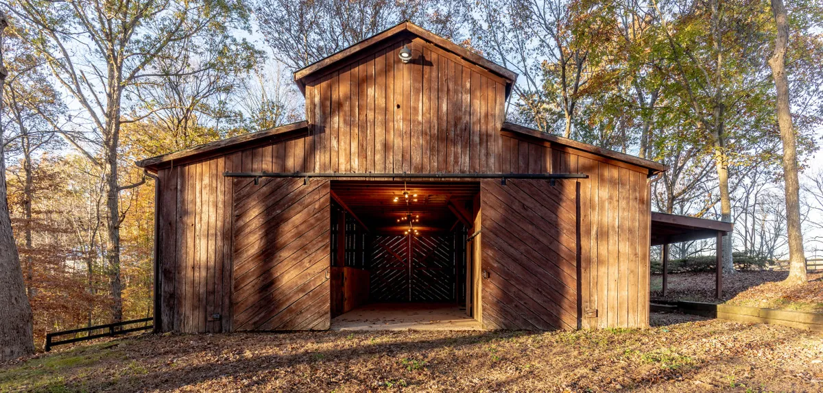 The hero image showcases a charming wooden barn structure with its doors open, surrounded by lush trees. The setting is tranquil, evoking a nostalgic countryside feel, and hints at spaces ideal for gatherings, creative pursuits, or relaxing at sunset.