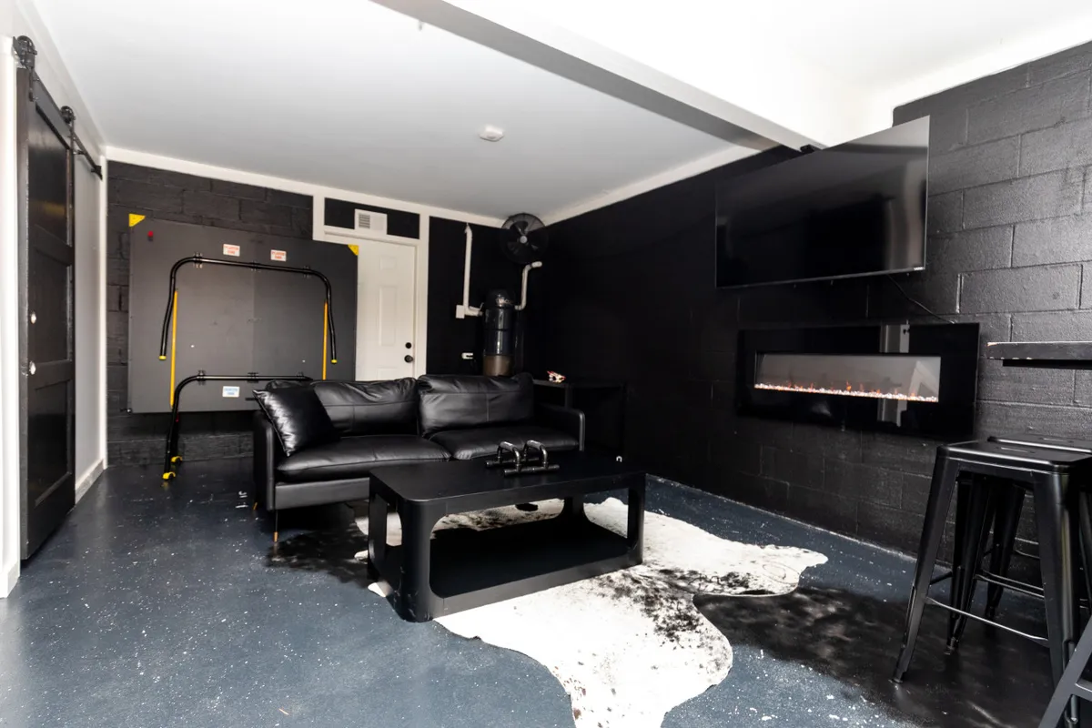 A contemporary and inviting lounge area with a black leather sofa, black coffee table, wall-mounted TV, and an electric fireplace. The setup is ideal for relaxing, watching TV, or enjoying cozy gatherings.